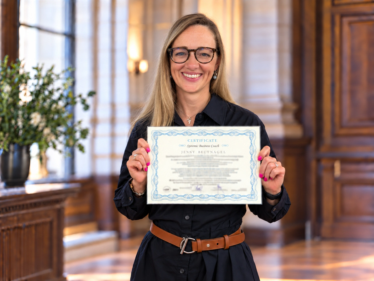 Jenny Beutnagel holding her Systemic Business Coach certificate in a staged formal setting.
